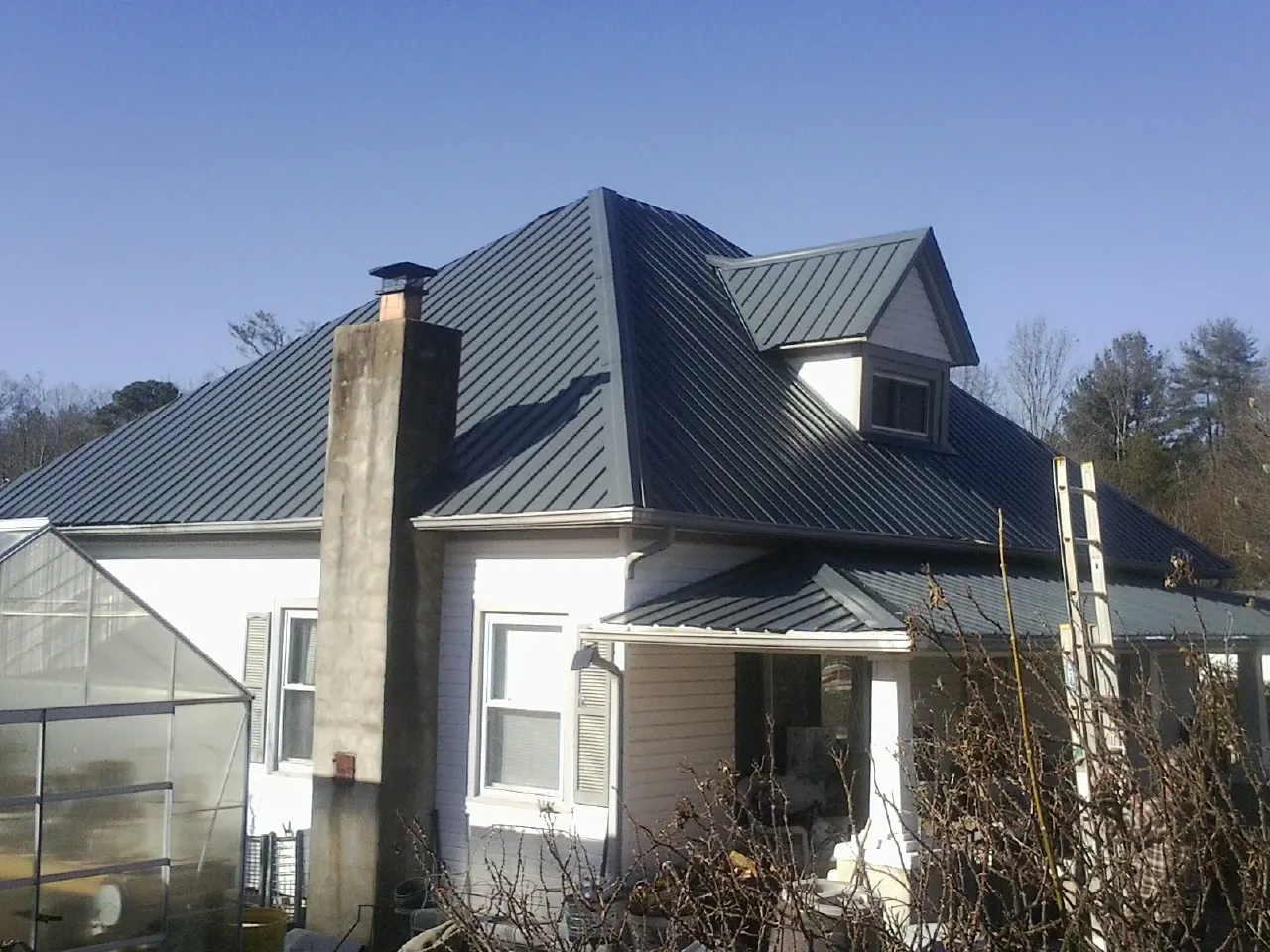 Dark blue standing seam metal roof on a white farmhouse with dormer — Slate & Tile Roof Repair by Roofing Brothers in Jessie