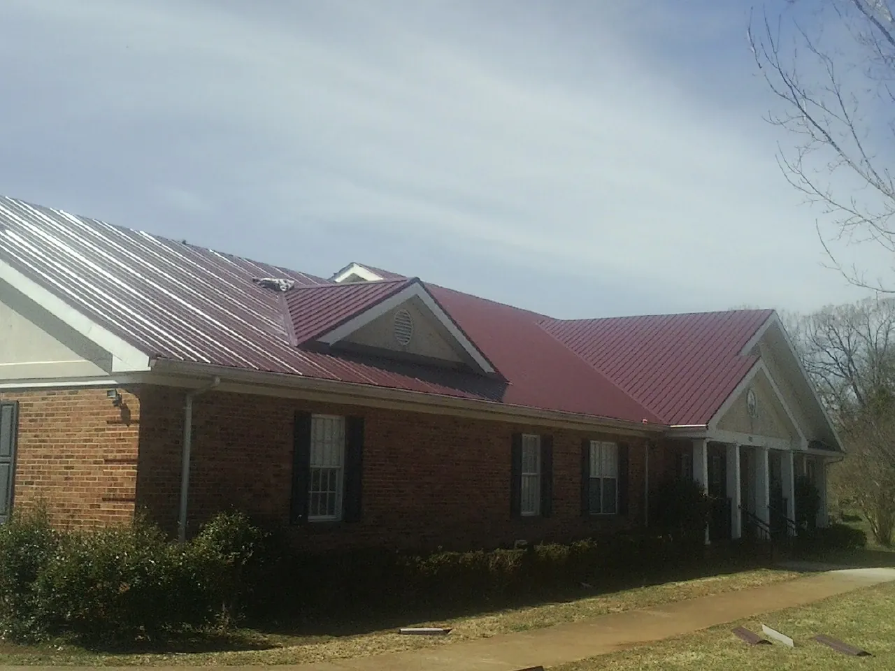 Red metal roof with gabled entries on a long brick building, from a Hail Damage Roof Repair job in Jessie