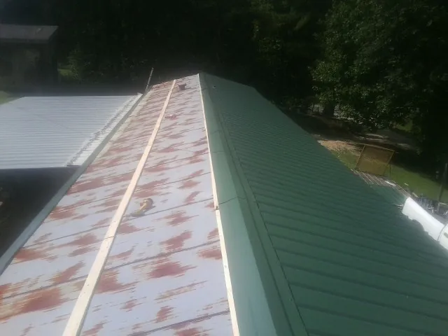 Old rusted panels beside newly installed green metal roofing — Wind Damage Roof Repair by Roofing Brothers in Jessie