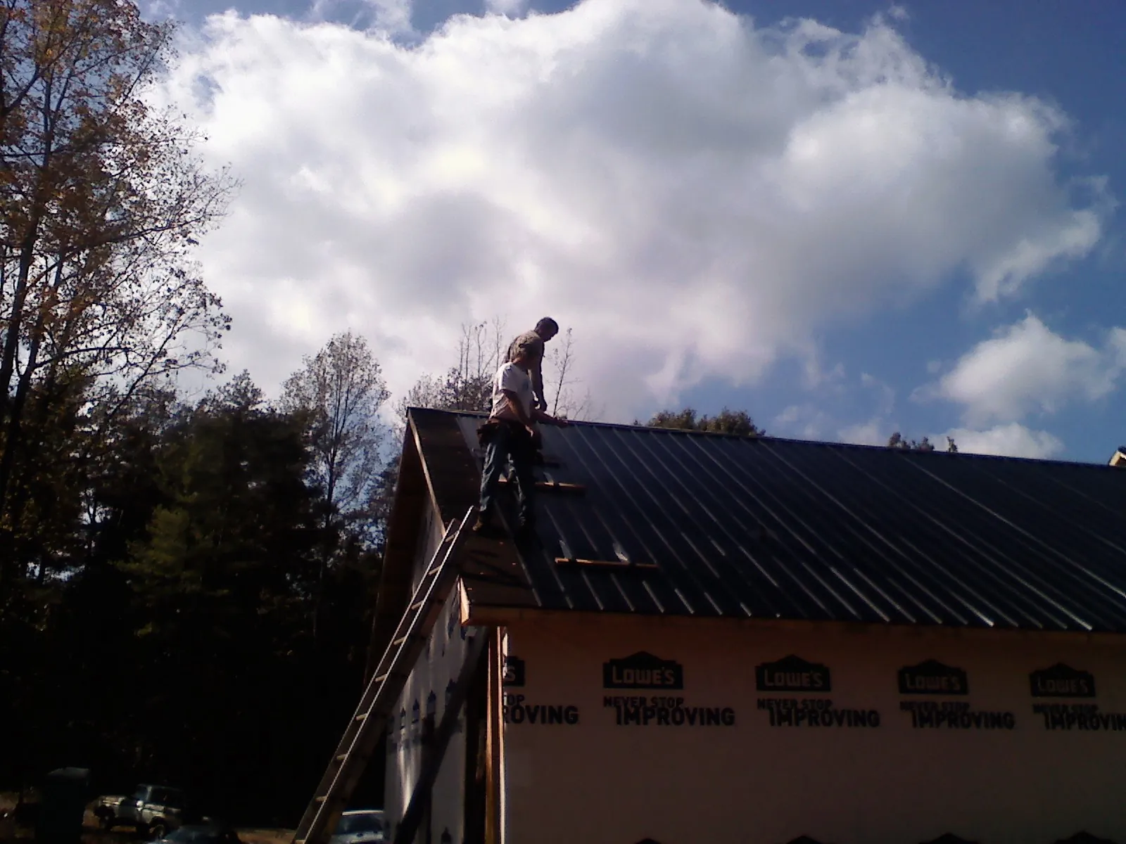 Roofer fastening dark metal panels high against a cloudy sky, from a Roof Inspection job in Jessie